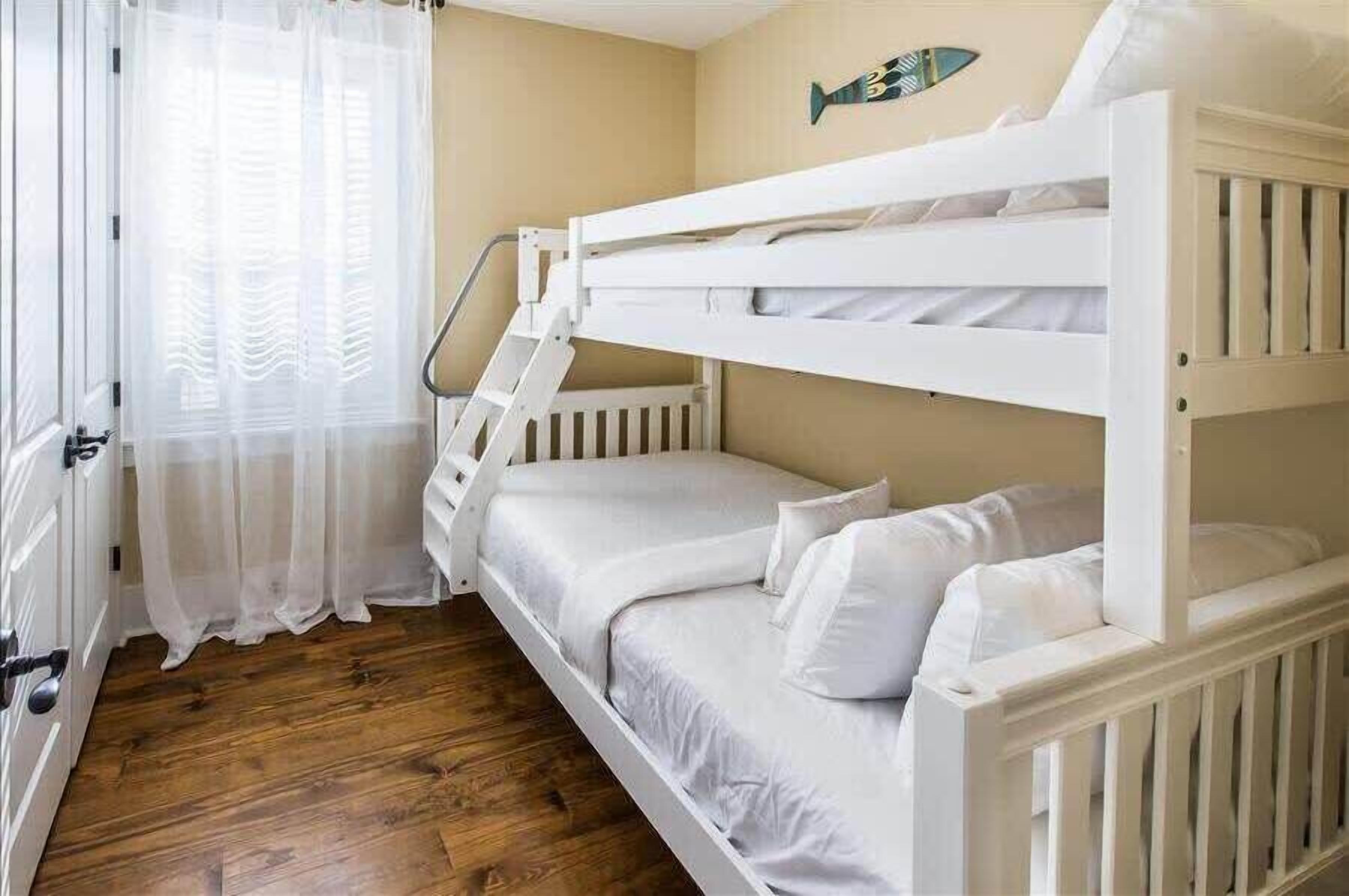 Habitació amb lliteres, roba de llit blanca, una decoració de peix a la paret i terra de fusta.