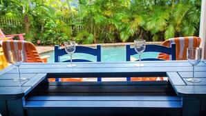 A poolside table with two chairs and two empty wine glasses, overlooking a swimming pool and lush greenery. - Sunset Landing AMI Beach House. 6BR/4.5BA. Private pool. 2 blks to beach. (Holmes Beach)