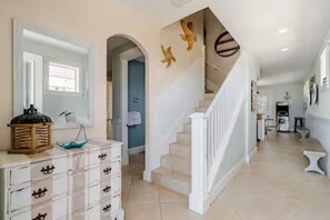 A hallway with a staircase, a white dresser with drawers, and a decorative wall piece.