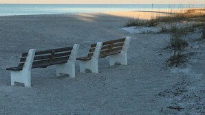 A bench on a sandy beach with the ocean in the background. - Sunset Landing AMI Beach House. 6BR/4.5BA. Private pool. 2 blks to beach. (Holmes Beach)