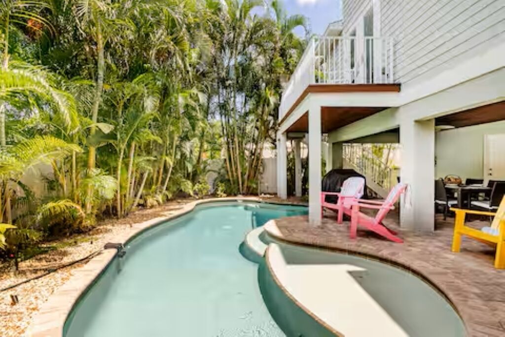Una piscina de borde curvo, rodeada de exuberante follaje y palmeras.