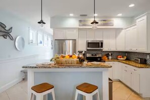 Cocina moderna con armarios blancos, una isla central con taburetes, electrodomésticos de acero inoxidable e iluminación colgante.
