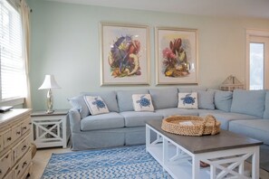 A living room with a grey sofa, a patterned rug, a white coffee table, and two framed botanical prints on the wall.