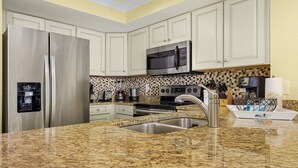 A kitchen with white cabinets, stainless steel appliances, a granite countertop, and a backsplash with a mosaic tile pattern. - Beachfront 10th Floor Resort Condo -  Breathtaking views  (Fort Myers)