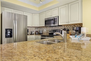 A kitchen with white cabinets, stainless steel appliances, a granite countertop, and a backsplash with a mosaic tile pattern. - Beachfront 10th Floor Resort Condo -  Breathtaking views  (Fort Myers)