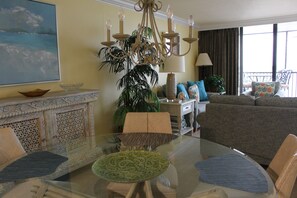 A living room with a glass coffee table, a sofa, a chandelier, and a painting on the wall.