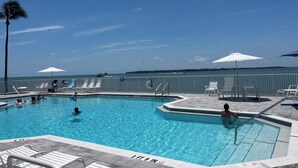 Une piscine à l’eau d’un bleu cristallin, entourée de chaises longues et de parasols, d’où l’on peut admirer l’océan et un navire au loin.