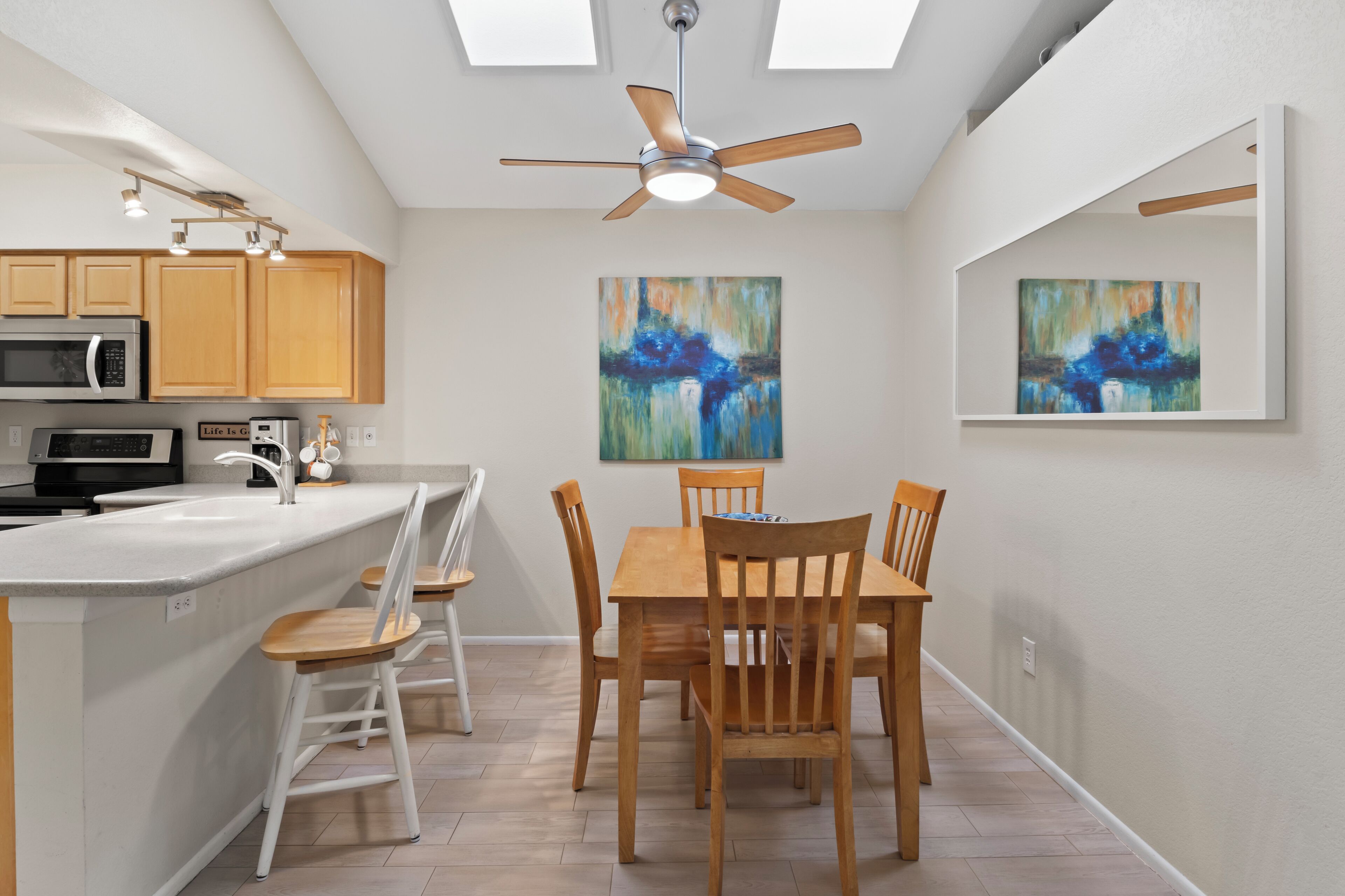 A modern kitchen with a central island, wooden chairs, and two abstract paintings on the walls.