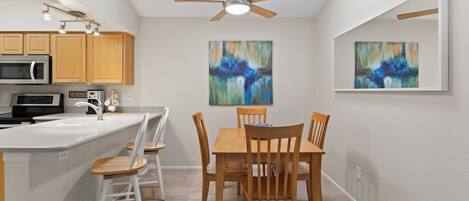A modern kitchen with a central island, wooden chairs, and two abstract paintings on the walls.