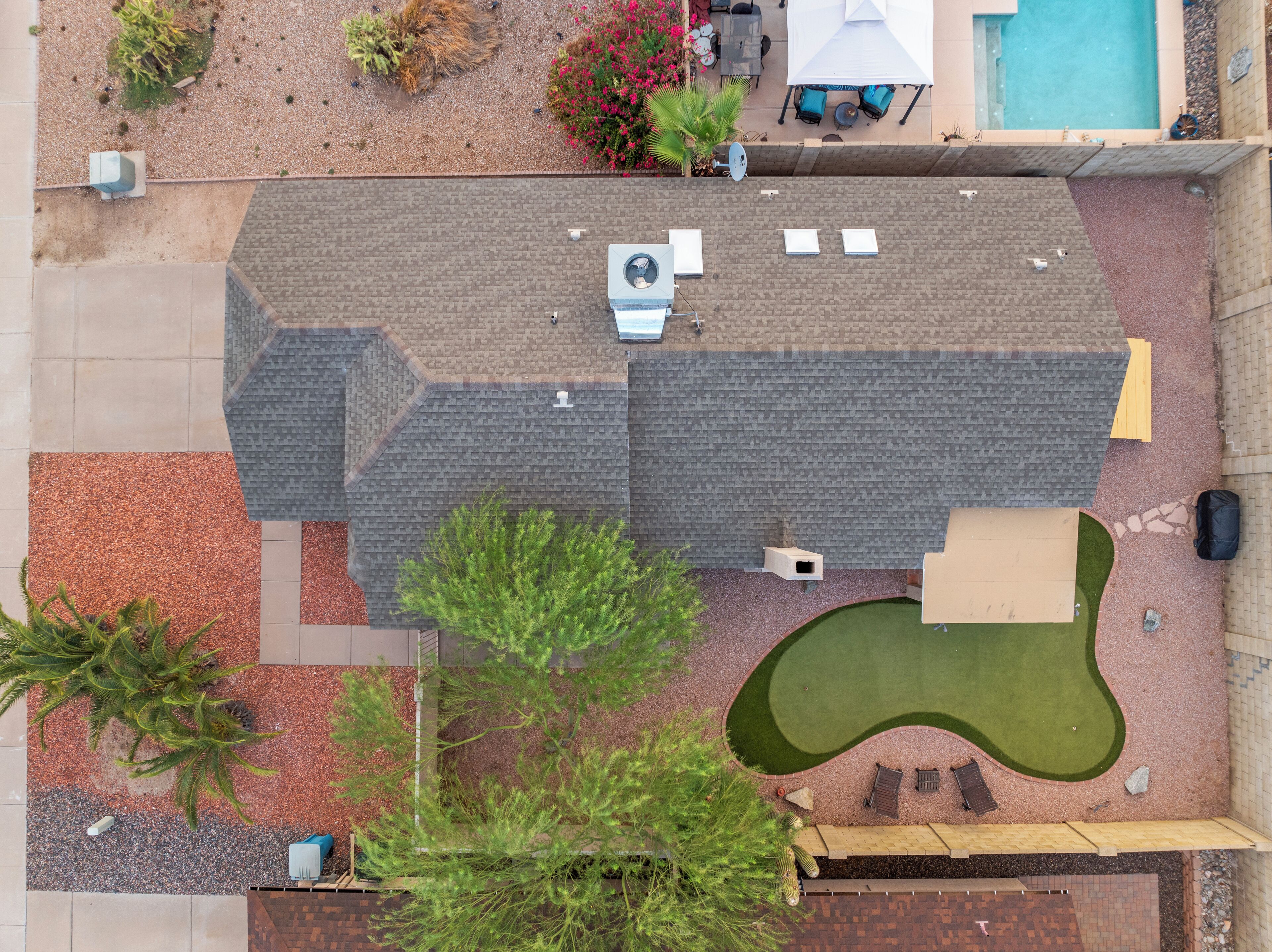 An aerial view of a residential property with a swimming pool, patio furniture, and a landscaped lawn.