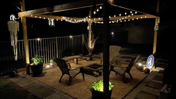 Un espace extérieur aménagé en terrasse, avec des guirlandes lumineuses, des meubles en bois et des plantes en pot.