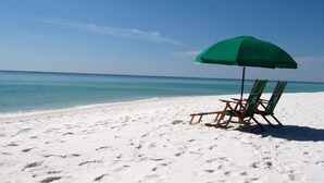 A beach with white sand and a green umbrella providing shade over two wooden beach chairs. - Islander Beach 2003 • 3BR 3BA, Amazing Direct Ocean View, Large Pool, Free Beach Service (Fort Walton Beach)