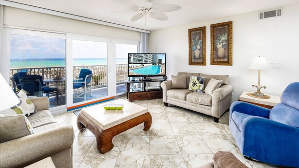 A living room with a TV, sofas, a coffee table, and a balcony with a view of the ocean. - Islander Beach 2003 • 3BR 3BA, Amazing Direct Ocean View, Large Pool, Free Beach Service (Fort Walton Beach)