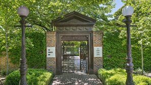 A brick entrance gate with a decorative arch and two street lamps on either side.