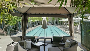 A covered outdoor seating area with a view of a swimming pool, surrounded by lounge chairs and umbrellas.