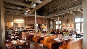 A spacious restaurant with wooden booths and tables, high ceilings, and pendant lighting.