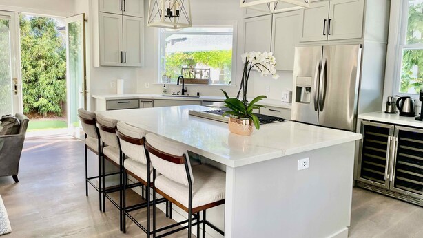 A modern kitchen with a large island, white cabinetry, stainless steel appliances, and a view of greenery outside.