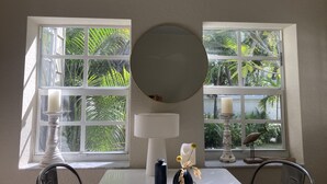 A room with a table, two windows with views of greenery, a round mirror, and a decorative bird statue. - DELRAY BEACH  Private Pool, Close To Sea (Delray Beach)