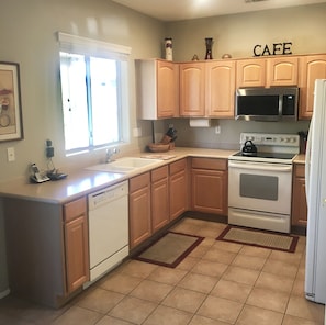 Una cocina con armarios de madera, microondas, horno, lavavajillas y un lavabo.
