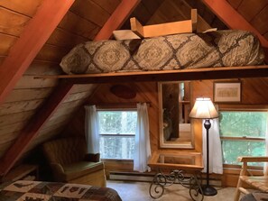 A cozy attic bedroom with a loft bed, a small table, a lamp, and a view of trees through the window. - FIELDSTONE AND LOG HOME ON BEECH.   
Ski season dates available at 2024 prices! (Beech Mountain)