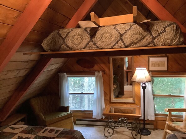 A cozy attic bedroom with a loft bed, a small table, a lamp, and a view of trees through the window. - FIELDSTONE AND LOG HOME ON BEECH.   
Ski season dates available at 2024 prices! (Beech Mountain)