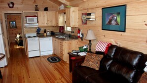A wooden cabin interior with a kitchen, dining area, and a living room with a leather couch.