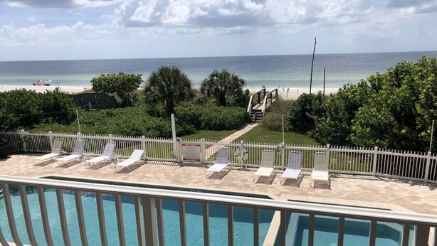 A swimming pool with lounge chairs and a view of the beach. - Beachfront Condo with Pool (Holmes Beach)