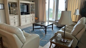 A living room with a sofa, armchair, coffee table, TV, and cabinets. - Beachfront Condo with Pool (Holmes Beach)