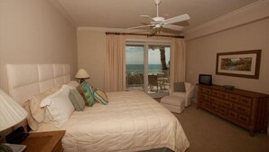 A hotel room with a bed, a chair, a dresser, a ceiling fan, and a view of the ocean through the window. - Beachfront Condo with Pool (Holmes Beach)