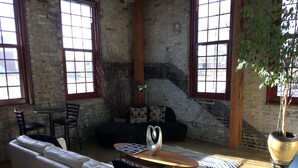 A spacious living room with a black sofa, a white sofa, a wooden coffee table, and a large potted plant.