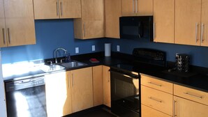 A compact kitchen with wooden cabinets, a black microwave, a dishwasher, and a sink.