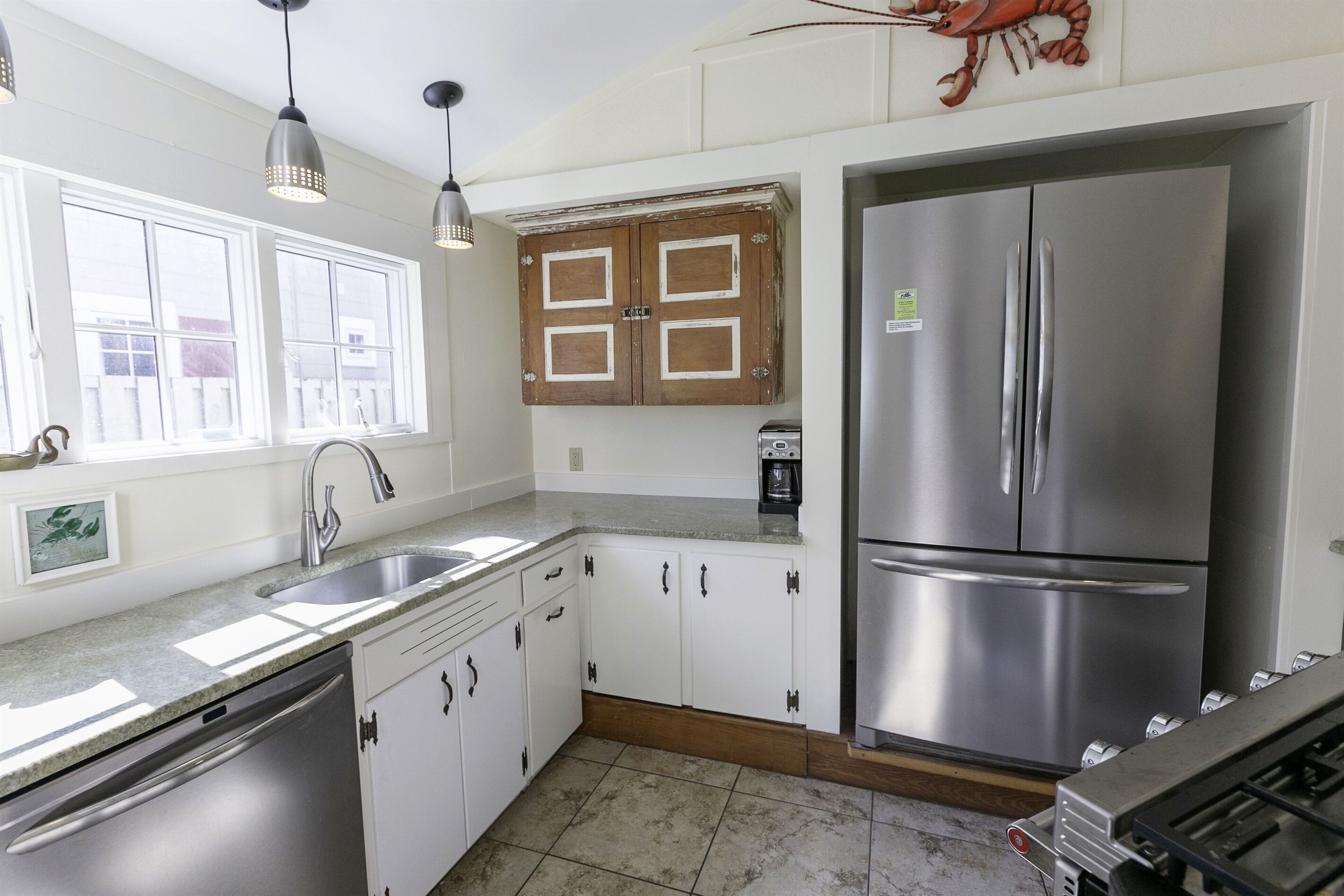 Cocina con armarios blancos, un refrigerador de acero inoxidable, un fregadero y luces colgantes.