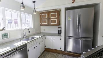 Cocina con armarios blancos, un refrigerador de acero inoxidable, un fregadero y luces colgantes.