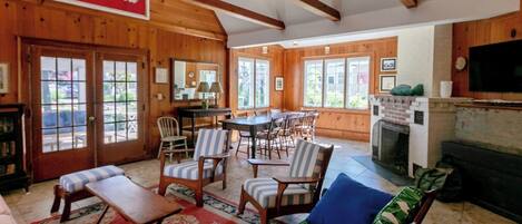 A cozy cabin interior with wooden walls, a dining area, a sofa, and a fireplace.