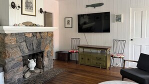 A living room with a stone fireplace, a television mounted on the wall, and a wooden floor.
