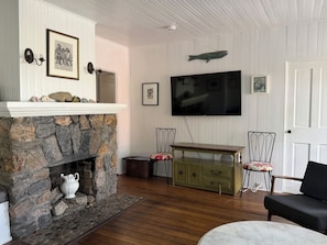 A living room with a stone fireplace, a television mounted on the wall, and a wooden floor.