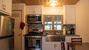 A compact kitchen with white cabinets, stainless steel appliances, and a wooden ceiling.