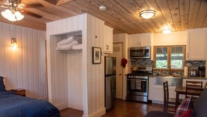 A cozy room with a bed, a sofa, a kitchen with appliances, and wooden walls.