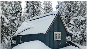 A snow-covered cabin with a steep roof, surrounded by snow-laden trees.