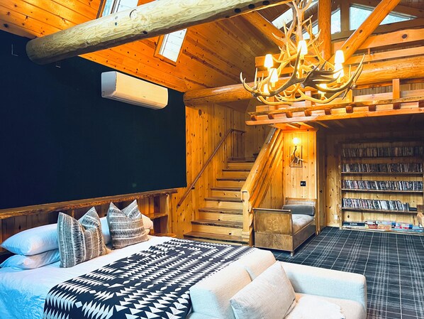 A cozy log cabin room with a bed, a sofa, a staircase, and a bookshelf filled with books.