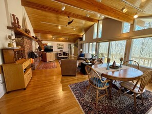 A spacious living area with wooden flooring, a dining table with chairs, a fireplace, and large windows offering a view of the outdoors. - Secluded Waterfront Location With Dock (Stonington)
