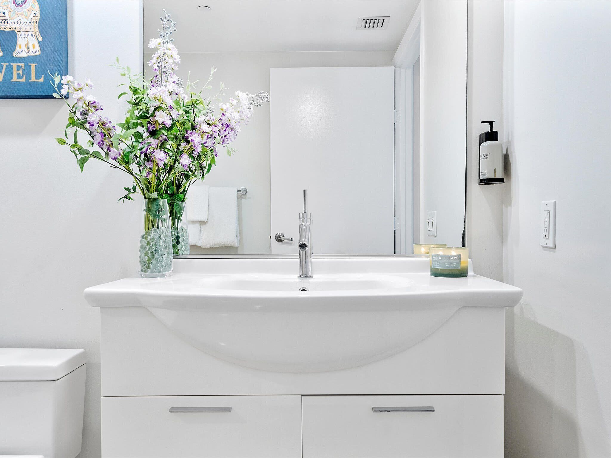 A bathroom with a white sink, a mirror, a towel rack, and a vase with flowers.