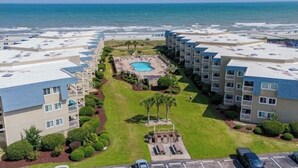 Ein Strandhotel mit mehreren Balkonen, einem zentral gelegenen Pool und Blick auf den Ozean.