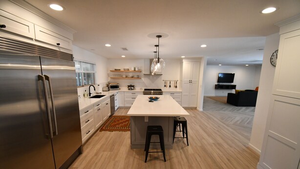 A modern kitchen with a central island, stainless steel appliances, and a dining area with a TV in the background. - Luxury Ranch House on Continental Golf Course, Great for families, Remodeled.  (Flagstaff)