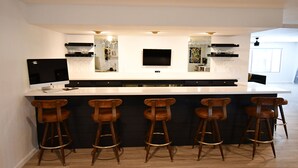 A modern kitchen with a central island, bar stools, a flat-screen TV, and wine glasses on shelves. - Luxury Ranch House on Continental Golf Course, Great for families, Remodeled.  (Flagstaff)