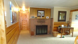 Ein gemütliches Wohnzimmer mit Kamin, Holzwänden, einem Esstisch und einer Treppe, die in einen anderen Raum führt.