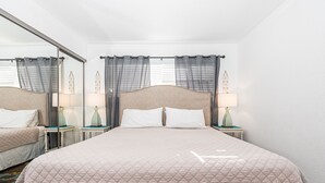 A hotel room with a large bed, two bedside tables with lamps, a mirror, and curtains. - Ocean View Corner Home (lower unit)  - 1 house from the Beach! - Walk to all the Hot Spots! (Newport Beach)