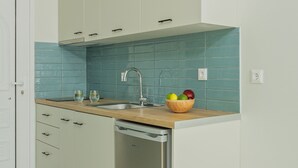 A compact kitchen with white cabinets, a stainless steel dishwasher, a wooden countertop, and a blue-tiled backsplash.