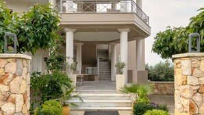 A two-story house with a balcony, stone pillars, and a variety of potted plants.