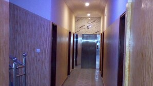 A long, narrow hallway with patterned flooring, a metal trash can, and a ceiling light. - Noahgarden (Cotonou)